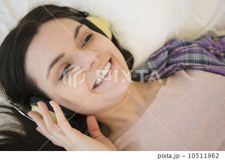 Portrait of young woman lying down on bed and listening to music 10511962