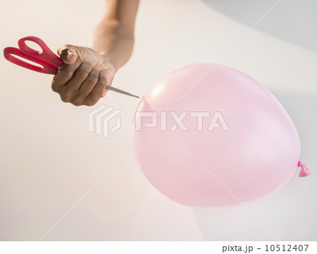 Close up of woman's hand popping balloon with scissors Close up of woman's hand popping balloon with scissors 10512407
