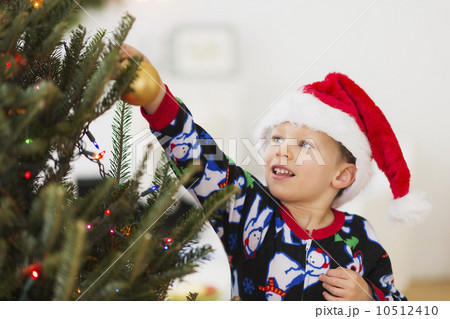 Boy (6-7) with santa hat decorating Christmas tree Boy (6-7) with santa hat decorating Christmas tree 10512410