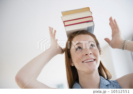 Teenage girl (14-15) holding stack of books on head 10512551