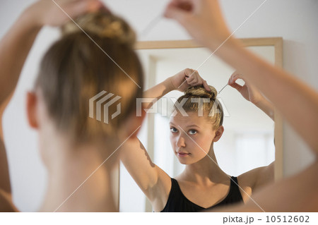 Rear view of teenage (16-17) ballerina looking into mirror and styling her hair 10512602