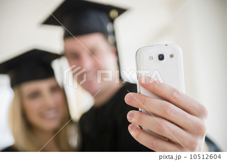 Couple of friends in graduation gowns taking photo with smartphone Couple of friends in graduation gowns taking photo with smartphone 10512604