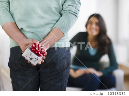 Young man with present behind his back, girlfriend in background Young man with present behind his back, girlfriend in background 10513335