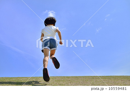 青空で走る女の子 後姿 の写真素材