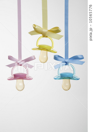 Baby pacifiers hanging from ribbons against a plain background. 10565776