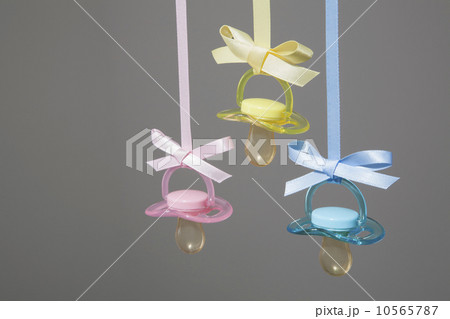 Baby pacifiers hanging from ribbons against a plain background. 10565787