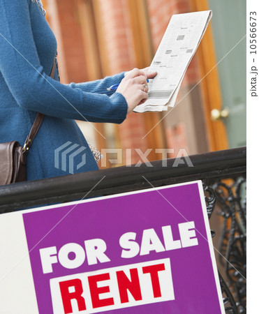 Close up of for sale sign with woman holding list in background 10566673