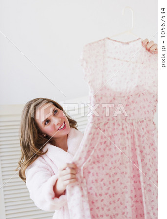 Young woman holding dress in bedroom Young woman holding dress in bedroom 10567634