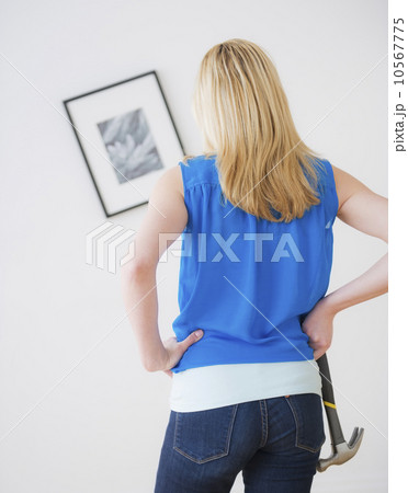 Rear view of woman holding hammer and looking at painting on wall 10567775