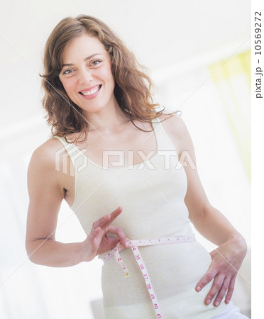 Young woman with tape measure wrapped around waist 10569272