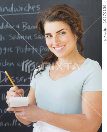 Portrait of smiling waitress against blackboard with menu 10570156