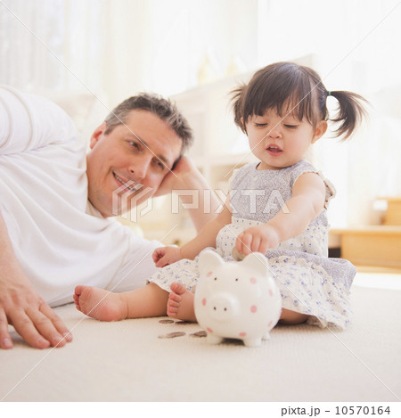 Baby girl (12-17 months) with father playing with piggy bank 10570164