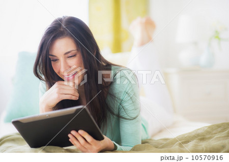 Portrait of woman lying down on bed using tablet pc Portrait of woman lying down on bed using tablet pc 10570916
