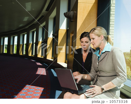 Businesswomen looking at laptop in office corridor Businesswomen looking at laptop in office corridor 10573316