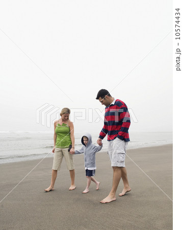 Parents holding hands with son on beach 10574434