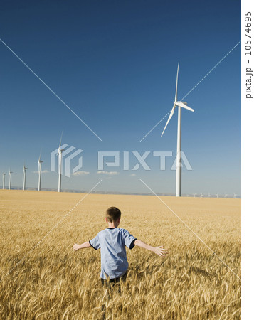 Boy running through field on wind farm Boy running through field on wind farm 10574695