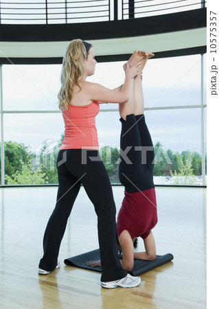 Yoga instructor helping woman with headstand pose Yoga instructor helping woman with headstand pose 10575357
