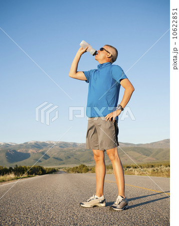 Mid adult an drinking water while taking break from running on empty road 10622851