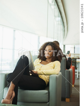 Smiling woman using digital tablet while waiting in lobby 10623341