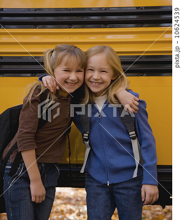Girls hugging in front of school bus 10624539
