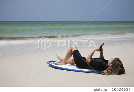 Girl looking at cell phone on surfboard, Florida, United States Girl looking at cell phone on surfboard, Florida, United States 10624657