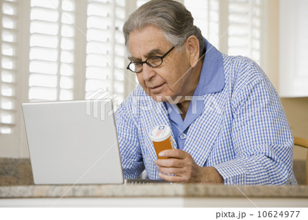 Senior man with medication bottle looking at laptop Senior man with medication bottle looking at laptop 10624977