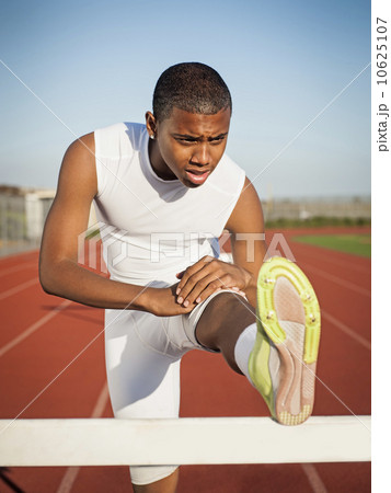 Boy (12-13) stretching on hurdle on running track 10625107