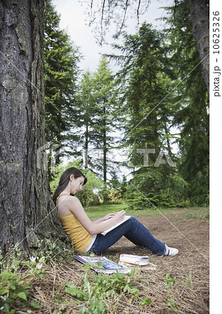 Girl leaning against tree writing in notebook 10625326