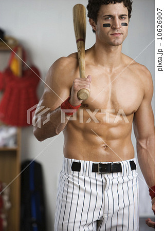 Portrait of baseball player with bare chest holding bat in locker room Portrait of baseball player with bare chest holding bat in locker room 10626907