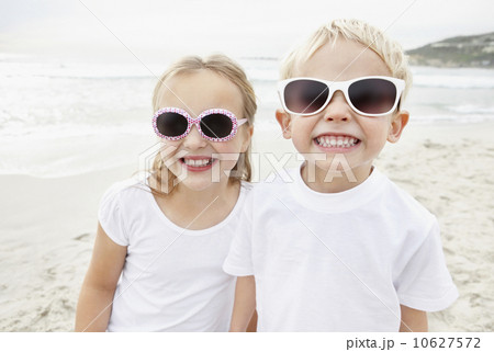 Portrait of brother (4-5) and sister (10-11) wearing sunglasses on beach 10627572