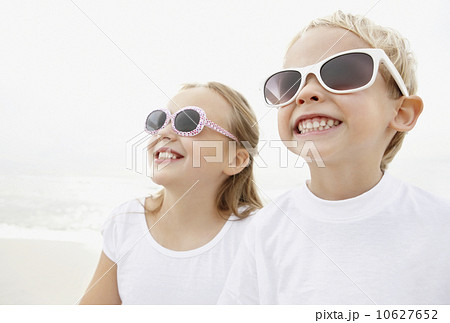 Portrait of brother (4-5) and sister (10-11) wearing sunglasses on beach 10627652