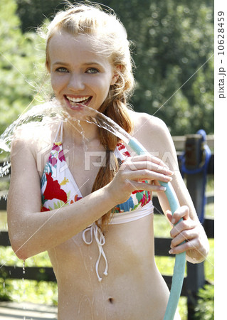 Teenage girl (14-15) wearing bikini drinking water from garden hose Teenage girl (14-15) wearing bikini drinking water from garden hose 10628459