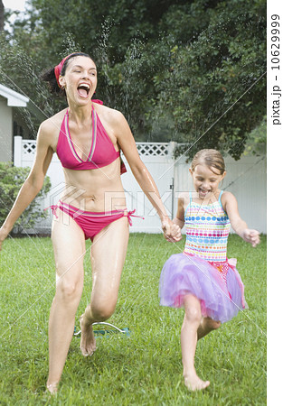Mother and daughter running through sprinkler 10629999
