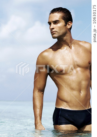 Sexy young man in swim trunks standing in the sea 10630175