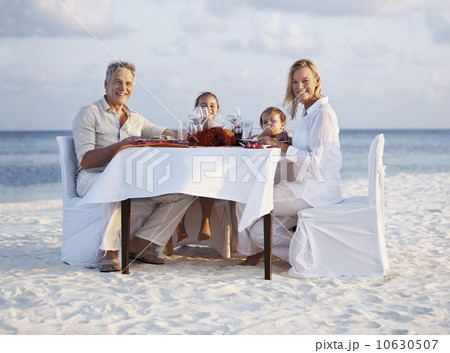 Portrait of parents with daughters (8-9), (4-5) sitting at table on beach Portrait of parents with daughters (8-9), (4-5) sitting at table on beach 10630507