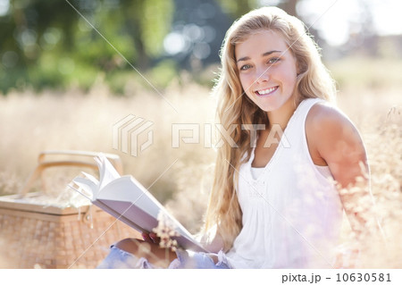 Teenage girl (16-17) posing for portrait while reading book outdoors Teenage girl (16-17) posing for portrait while reading book outdoors 10630581