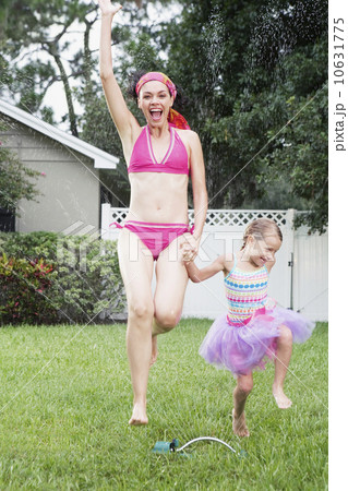 Mother and daughter running through sprinkler 10631775