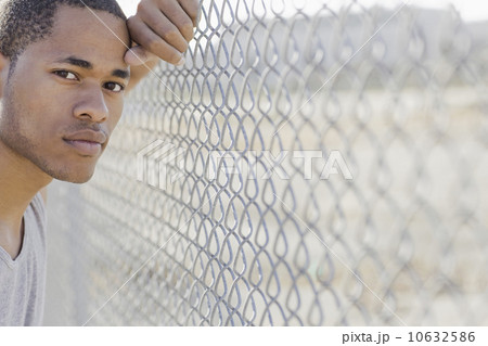 Portrait of young man leaning against chain-link fence 10632586