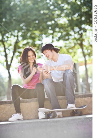 Young multi-racial couple sitting with skateboard, using mobile phone Young multi-racial couple sitting with skateboard, using mobile phone 10632655