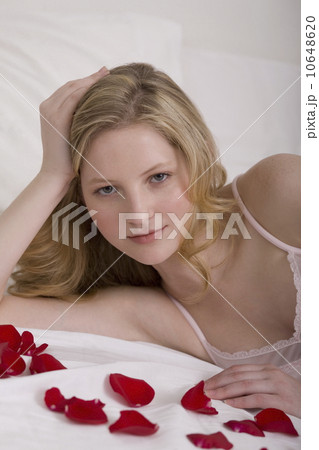 Young woman laying in bed with flower pedals Young woman laying in bed with flower pedals 10648620
