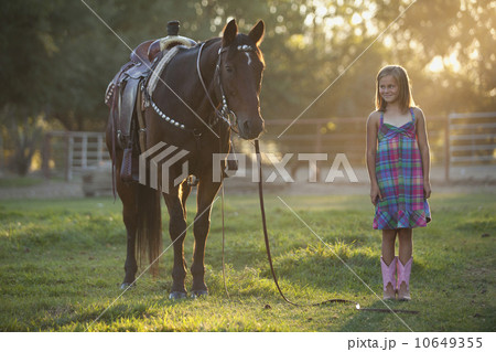 Girl (8-9) standing with horse in paddock 10649355