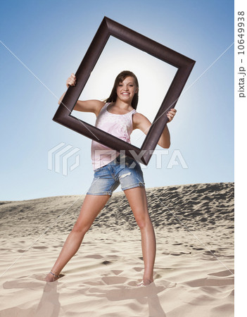 Woman standing on beach holding picture frame 10649938