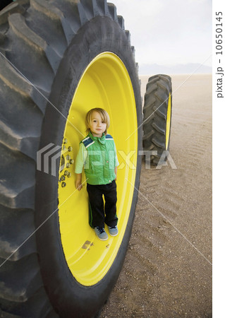 Boy (2-3) standing in tractor wheel 10650145