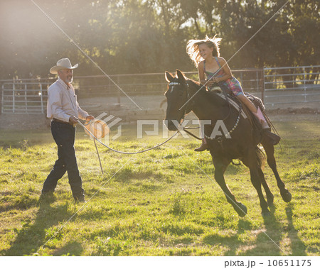 Trainer assisting girl (8-9) riding horse in paddock 10651175