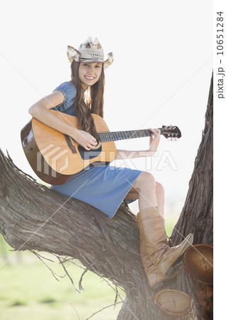 Cowgirl sitting in tree playing guitar Cowgirl sitting in tree playing guitar 10651284