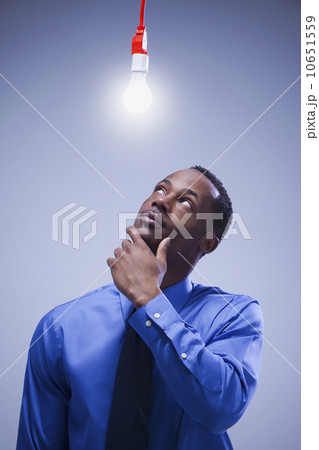 Contemplative businessman standing under a light bulb 10651559