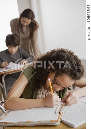 Writing girl (10-11) with boy (12-13) and teacher in background Writing girl (10-11) with boy (12-13) and teacher in background 10661348