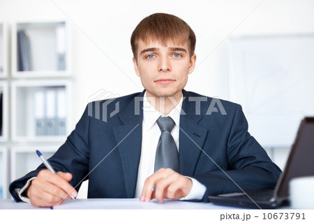 Portrait of young smiling business man writing on paperwork in o 10673791