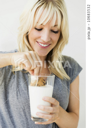 Studio portrait of blonde woman dipping cookie in milk 10683532