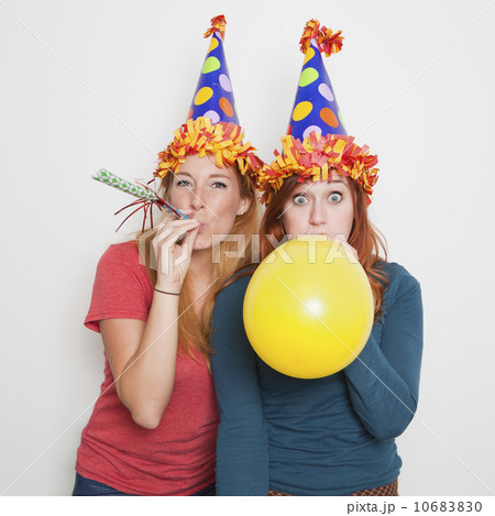 Studio Shot, Two women wearing party hats and one blowing up yellow balloon 10683830